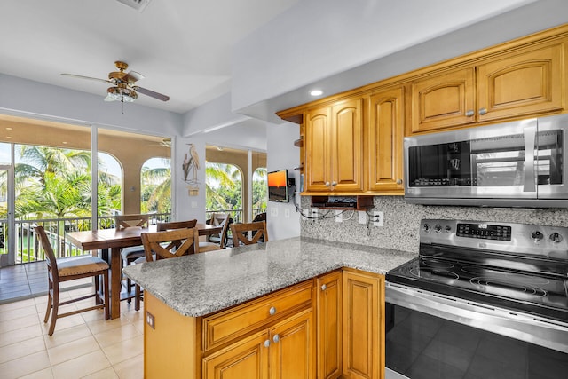 kitchen with light tile patterned floors, stainless steel appliances, backsplash, brown cabinetry, and a peninsula