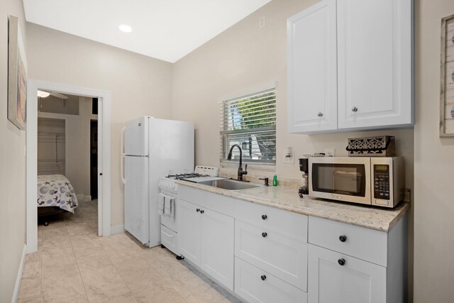 kitchen featuring white appliances, baseboards, light stone counters, white cabinetry, and a sink