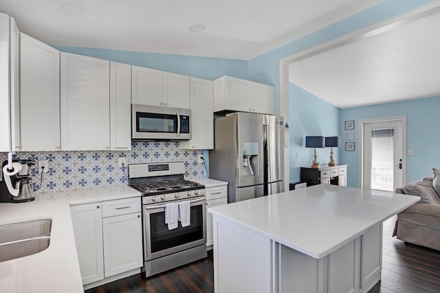 kitchen featuring light countertops, backsplash, appliances with stainless steel finishes, open floor plan, and white cabinetry