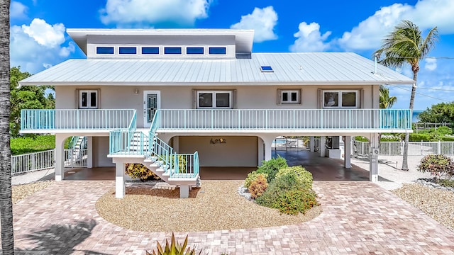 view of front facade featuring metal roof, stairs, decorative driveway, stucco siding, and a carport