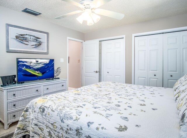 bedroom featuring a ceiling fan, a textured ceiling, visible vents, and two closets