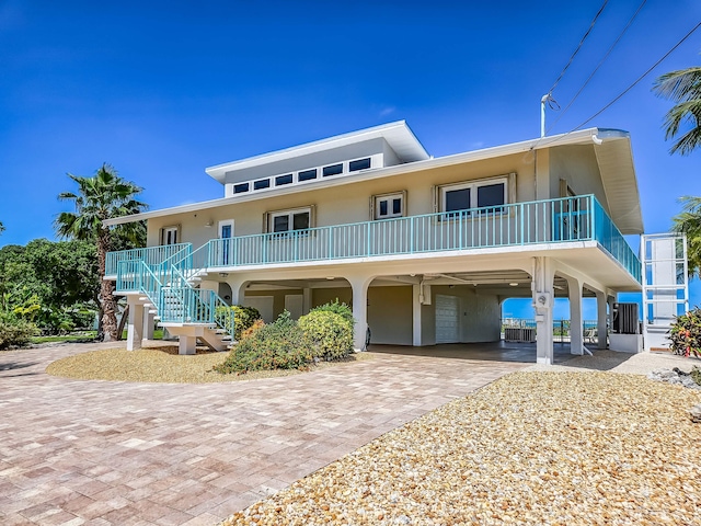 raised beach house with a carport, driveway, stairway, and stucco siding