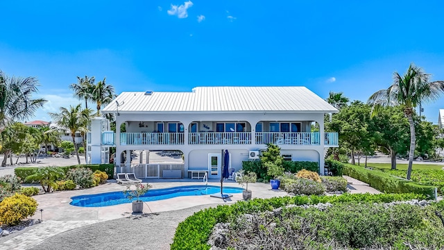 rear view of property featuring an outdoor pool, a balcony, metal roof, a patio area, and stucco siding