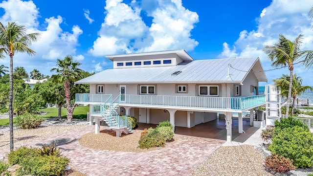 rear view of house featuring metal roof, covered porch, stairs, decorative driveway, and a carport