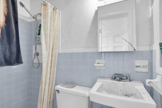 bathroom with tile walls, toilet, a tile shower, and a sink