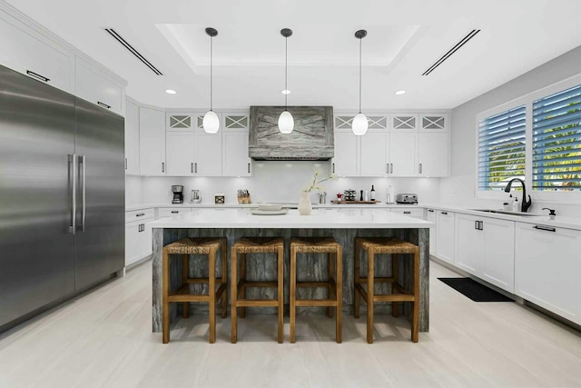 kitchen with a sink, a raised ceiling, stainless steel built in refrigerator, and light countertops
