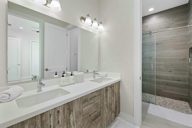 full bathroom featuring double vanity, a stall shower, baseboards, and a sink