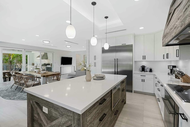 kitchen with a kitchen island, light countertops, built in appliances, white cabinetry, and wall chimney range hood