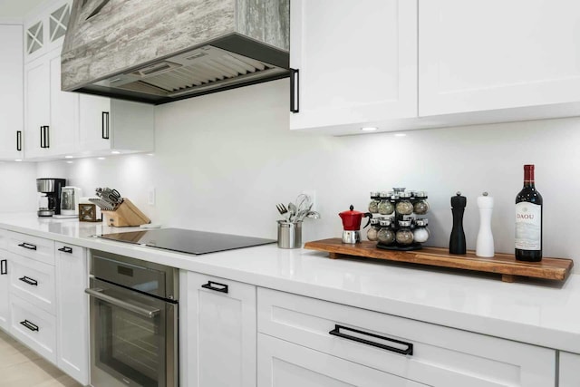kitchen featuring oven, premium range hood, white cabinetry, light countertops, and black electric cooktop