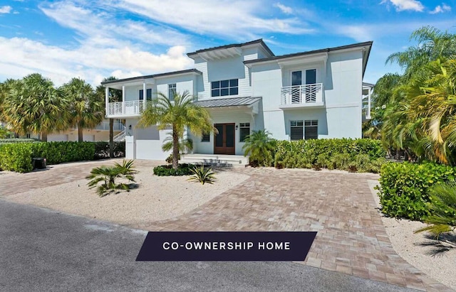 view of front facade featuring stucco siding, decorative driveway, french doors, metal roof, and a balcony