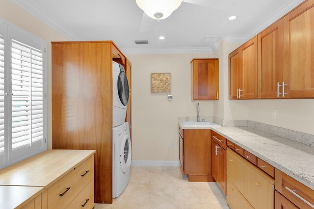 washroom featuring a sink, stacked washer / drying machine, cabinet space, and crown molding