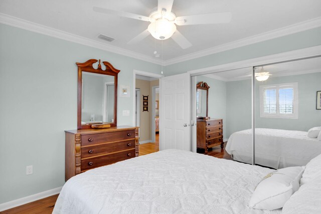 bedroom with visible vents, crown molding, baseboards, wood finished floors, and a closet