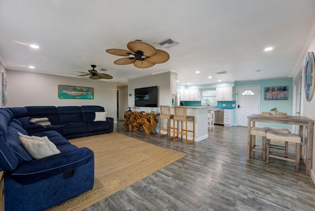 living area with ornamental molding, wood finished floors, visible vents, and recessed lighting