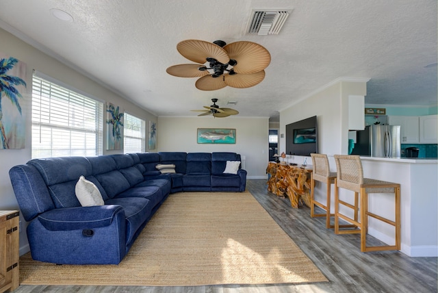 living area with a textured ceiling, visible vents, wood finished floors, and ornamental molding