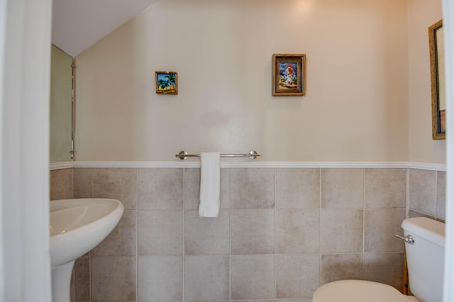 half bath featuring tile walls, toilet, wainscoting, and a sink