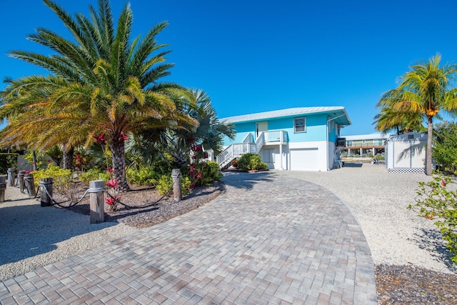 view of front facade featuring stairway, metal roof, an attached garage, decorative driveway, and stucco siding