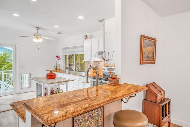 kitchen with under cabinet range hood, a peninsula, white cabinets, and stainless steel range with electric cooktop