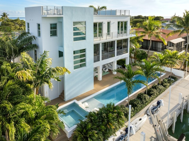 rear view of property with a balcony, an outdoor pool, and stucco siding