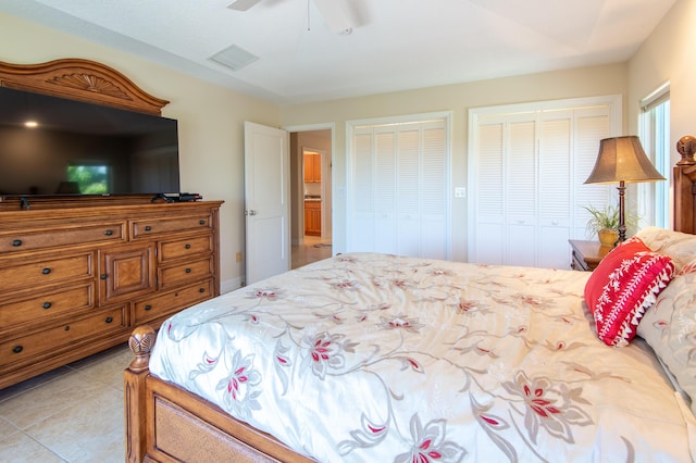 bedroom with light tile patterned floors, visible vents, two closets, and a ceiling fan