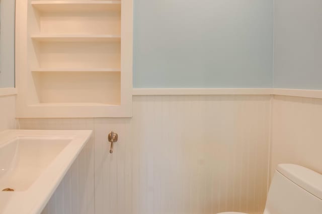 half bathroom with built in shelves, wainscoting, and toilet