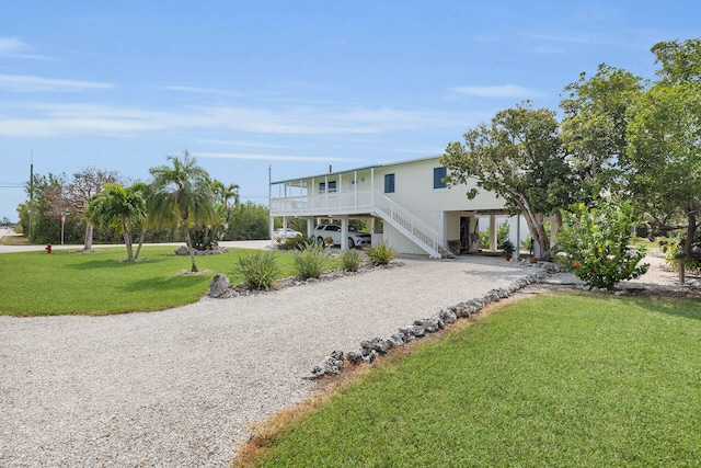 beach home with a front yard, gravel driveway, covered porch, stairs, and a carport