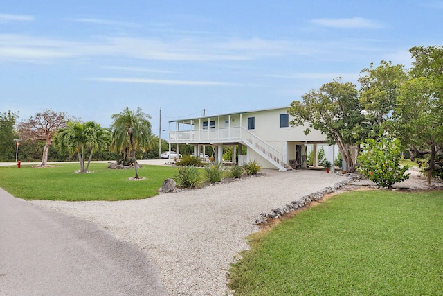 raised beach house with gravel driveway, a front lawn, stairs, covered porch, and a carport