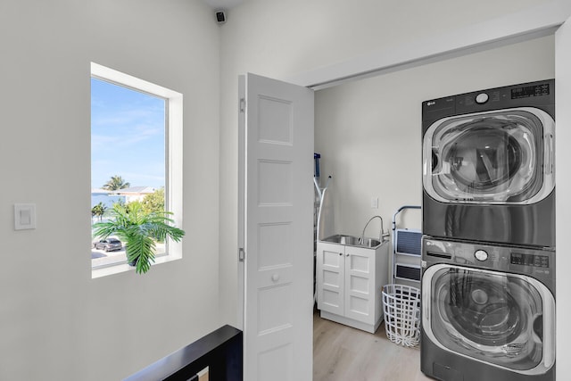 clothes washing area with a sink, light wood-type flooring, stacked washing maching and dryer, and laundry area