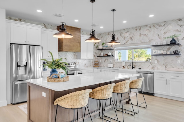 kitchen with light wood-type flooring, open shelves, a kitchen island, appliances with stainless steel finishes, and backsplash