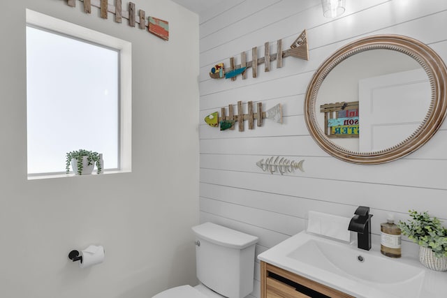 bathroom with wood walls, vanity, and toilet