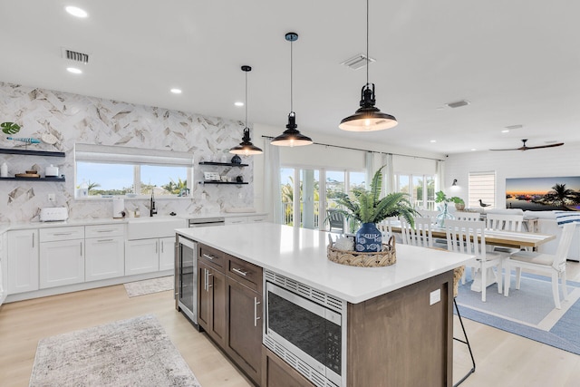kitchen featuring stainless steel microwave, light wood-type flooring, open shelves, and a healthy amount of sunlight