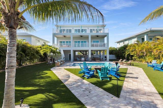 rear view of property with a yard, a ceiling fan, a patio area, a balcony, and an outdoor pool