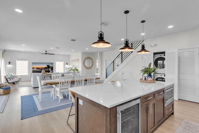 kitchen with stainless steel microwave, stacked washer and clothes dryer, open floor plan, light wood-style floors, and beverage cooler