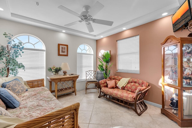 living area with a tray ceiling, recessed lighting, a ceiling fan, and baseboards