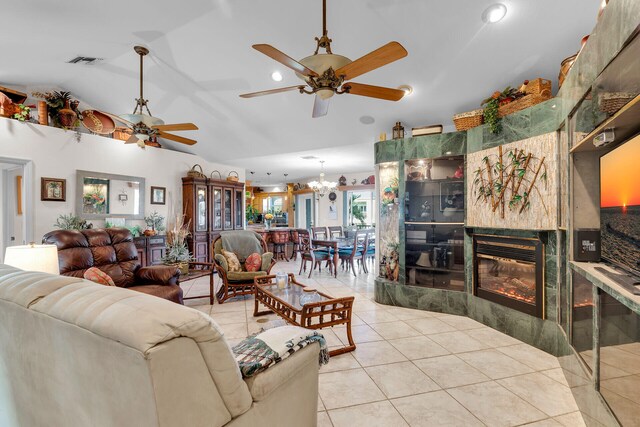 living room featuring lofted ceiling, visible vents, a high end fireplace, light tile patterned flooring, and ceiling fan with notable chandelier