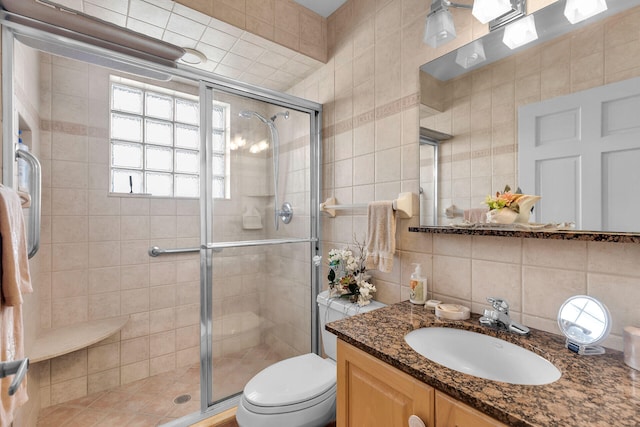 bathroom featuring tile walls, backsplash, toilet, a shower stall, and vanity