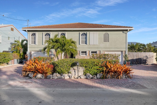 view of front of home featuring decorative driveway, a tile roof, stucco siding, an attached garage, and fence