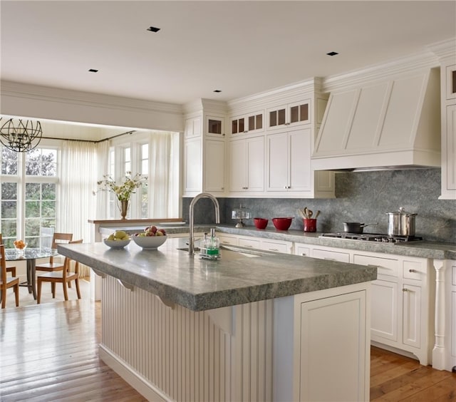 kitchen featuring light hardwood / wood-style floors, custom range hood, and a kitchen island with sink