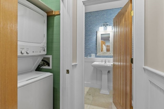 clothes washing area featuring sink, light tile patterned floors, and stacked washing maching and dryer