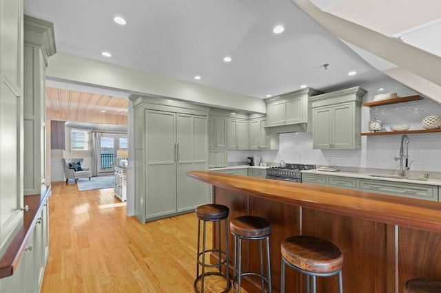 kitchen featuring stainless steel gas stove, sink, wooden counters, backsplash, and light wood-type flooring