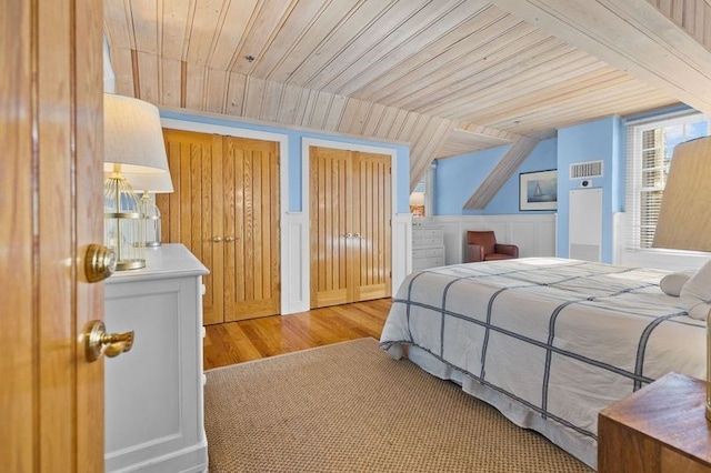 bedroom with wooden ceiling, lofted ceiling, light wood-type flooring, and multiple closets