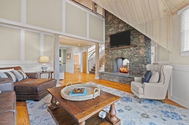 living room with light wood-type flooring, high vaulted ceiling, a stone fireplace, and wood ceiling