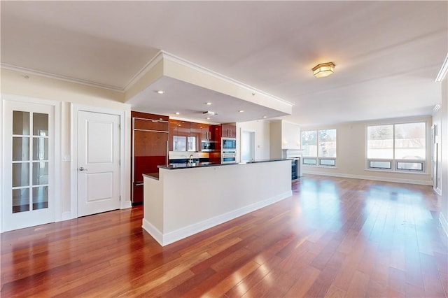 kitchen with hardwood / wood-style floors, stainless steel microwave, crown molding, and an island with sink