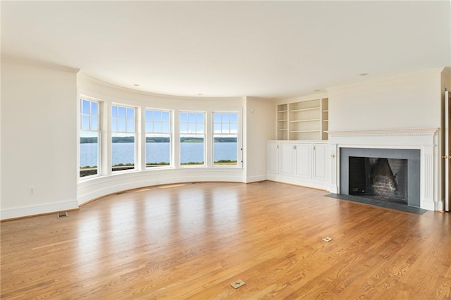 unfurnished living room with a water view, ornamental molding, built in shelves, and light hardwood / wood-style floors