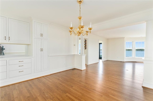 unfurnished room featuring crown molding, a chandelier, decorative columns, and light hardwood / wood-style flooring