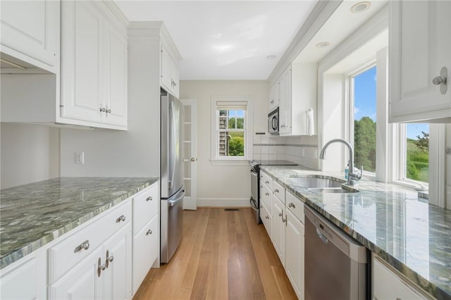 kitchen featuring sink, white cabinetry, light hardwood / wood-style flooring, dark stone countertops, and appliances with stainless steel finishes