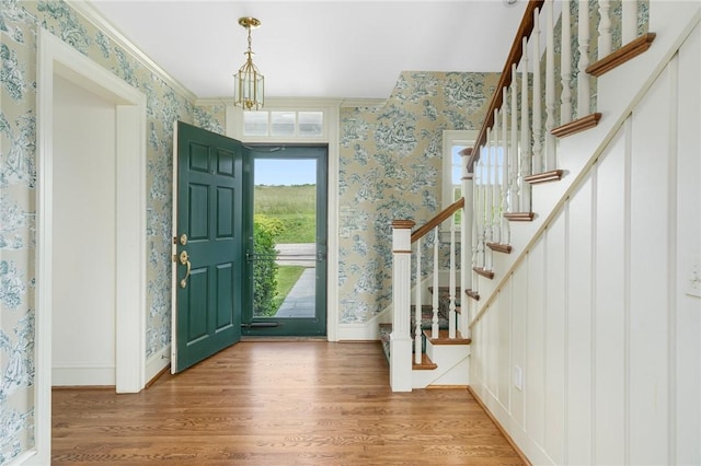 foyer with an inviting chandelier, ornamental molding, and wood-type flooring