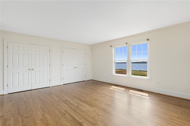 unfurnished bedroom featuring two closets, light hardwood / wood-style flooring, and a water view