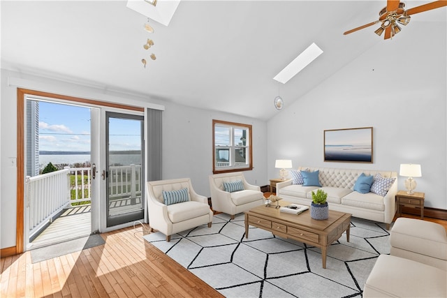 living room with light wood-type flooring, ceiling fan, a skylight, and high vaulted ceiling