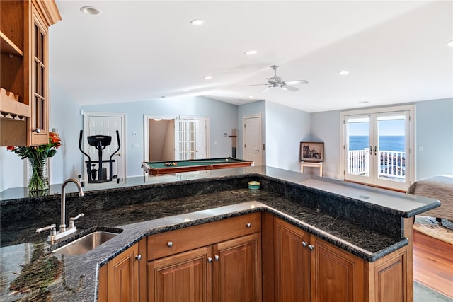 kitchen with ceiling fan, a water view, sink, pool table, and dark stone countertops