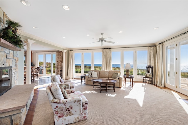 living room with a stone fireplace, ceiling fan, decorative columns, and a water view